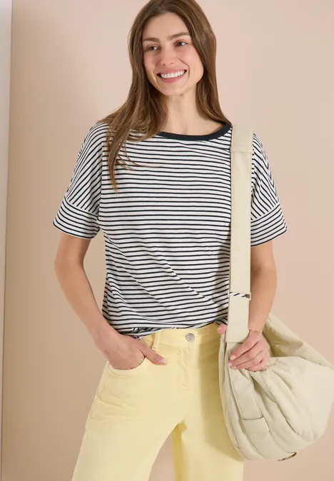 Frau trägt gestreiftes Shirt, breite gelbe Hose und großen gesteppten Beutel.