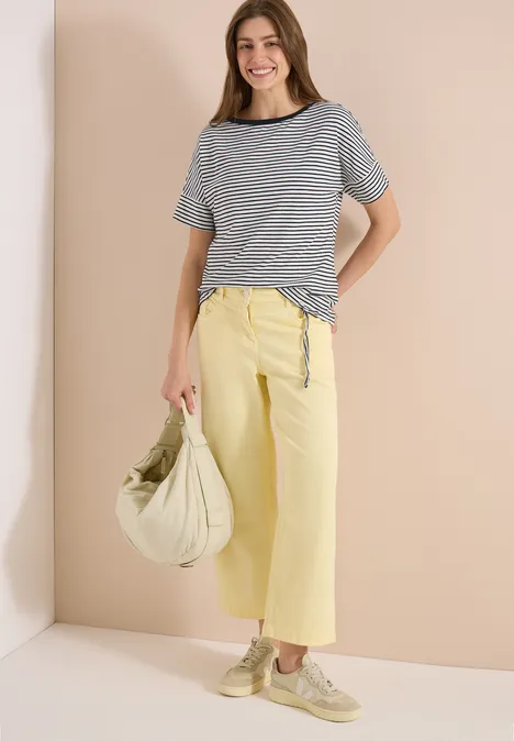 Frau trägt gestreiftes Kurzarmshirt und gelbe weite Culotte, dazu helle Tasche und Schuhe.