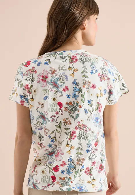 Frau trägt weißes T-Shirt mit kurzen Ärmeln und buntem Blumenmuster auf der Rückseite.