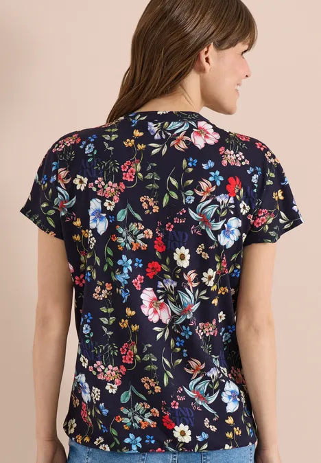 Een persoon van achteren in een donkerblauw T-shirt met gekleurde bloemenprint.