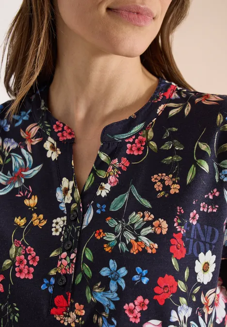 Vrouw draagt in close-up een donkerblauwe top met kleurrijk bloemenpatroon en knoopsluiting.