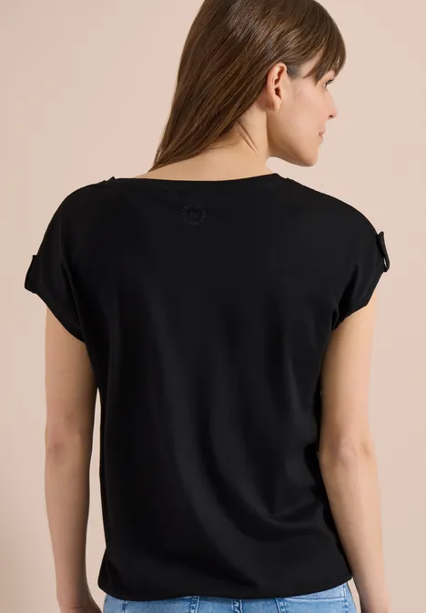 Dame von hinten in schwarzem, lockerem T-Shirt vor einfarbigem Hintergrund.