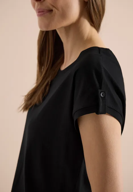 Eine Frau trägt ein schwarzes T-Shirt mit hochgekrempelten Ärmeln.