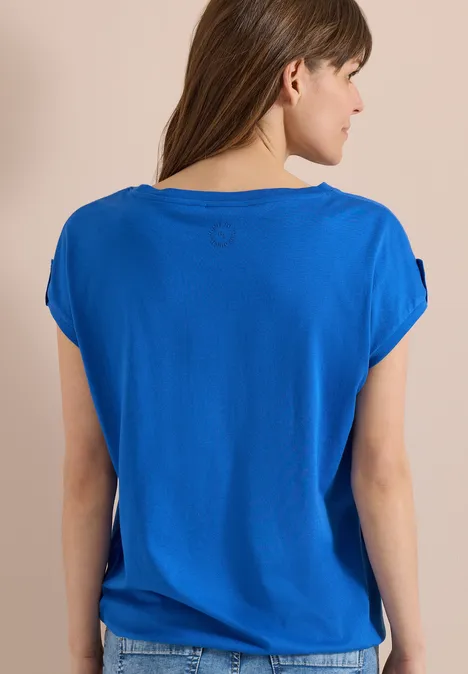 Achteraanzicht van een vrouw in een loszittend blauw t-shirt met korte mouwen.
