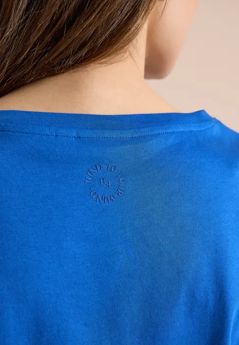 Achteraanzicht van persoon met helderblauw T-shirt en klein rond logo in de nek.