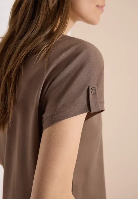 Zijaanzicht van een vrouw in een bruin T-shirt met korte mouwen en knoopdetail