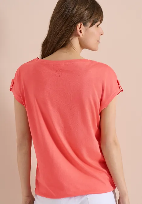 Rückenansicht eines korallenroten, kurzärmeligen Oberteils an einer Frau.