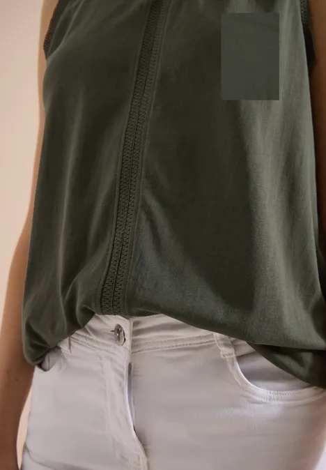 Portrait von Oberkörper mit olivgrünem, geknotetem Top und weißer Jeanshose.