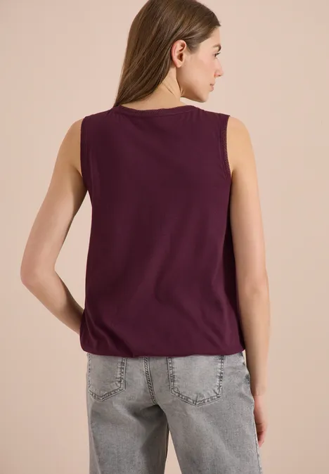 Frau von hinten in ärmellosem lila Oberteil und grauen Jeans
