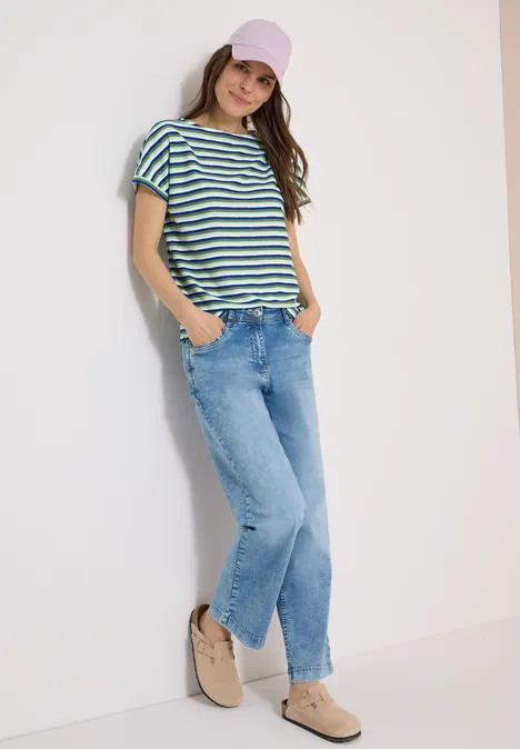 Gestreept shirt met structuur null Een vrouw leunt tegen een muur, draagt een gestreept T-shirt, spijkerbroek en comfortabele schoenen.