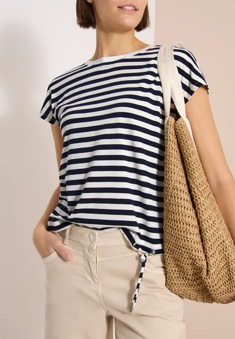 Femme en marinière blanche et bleue, pantalon clair et grand sac en paille.