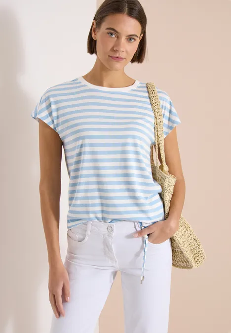 Frau in blau-weiß gestreiftem T-Shirt, weißer Hose und Strohtasche.