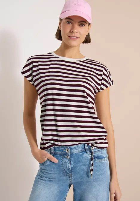 Femme en t-shirt rayé noué à la taille, jean et foulard rose, visage flouté.