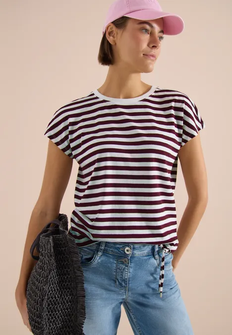 Femme en T-shirt rayé blanc et foncé à manches courtes, jean bleu clair, sac en maille et casquette.