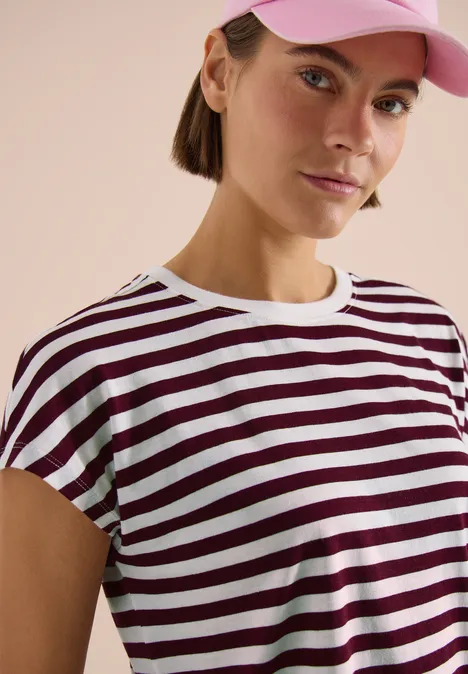 Buste d'une personne portant un T-shirt rayé blanc et bordeaux, fond neutre.