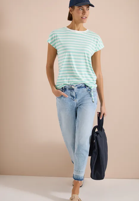 Femme en t-shirt rayé vert menthe et blanc, jean clair retroussé, tenant une veste foncée.