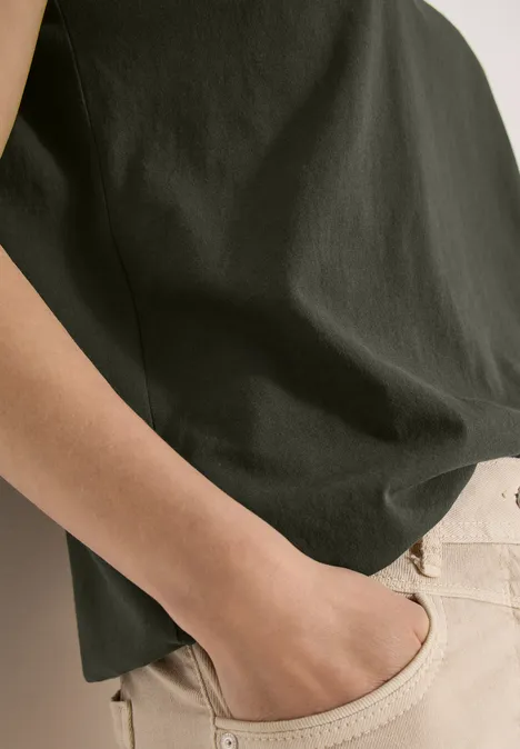 Une personne porte un t-shirt sombre et un pantalon clair, main détendue dans la poche.