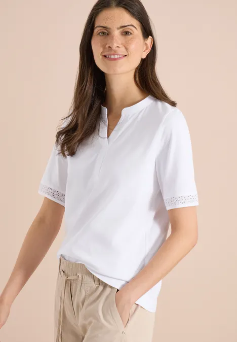 Frau in weißem Shirt mit Spitzenärmeln und beiger Hose.