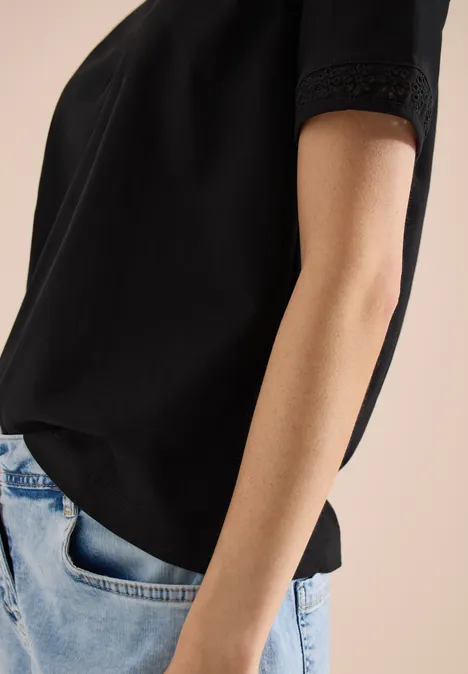 Vrouw in zwart T-shirt en spijkerbroek, hand nonchalant in de zak.