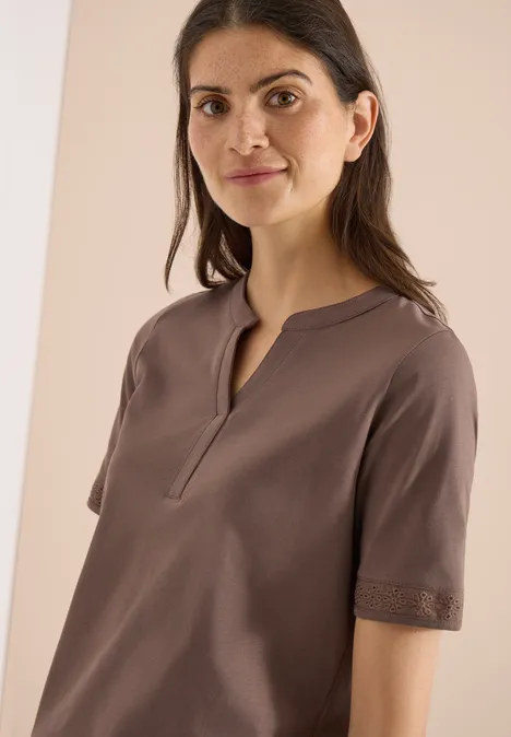 Frau trägt schlichtes, kurzärmeliges, braunes Oberteil mit kleinem V-Ausschnitt und Spitzenbesatz