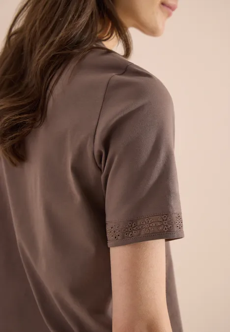 Seitenansicht einer Frau in braunem Kurzarmshirt mit dekorativem Ziersaum.
