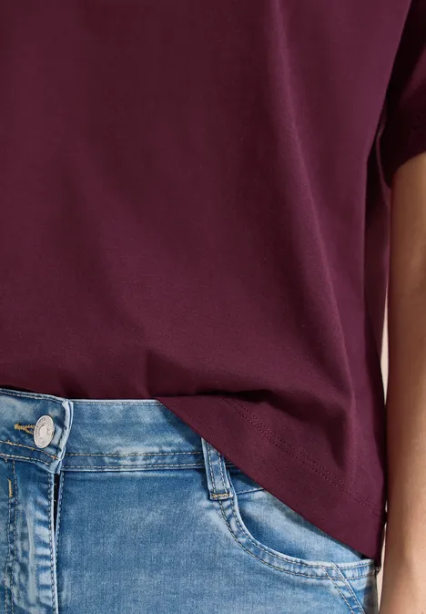 Close-up van een persoon met een donkerrood T-shirt, gedeeltelijk in een lichtblauwe jeans gestoken.