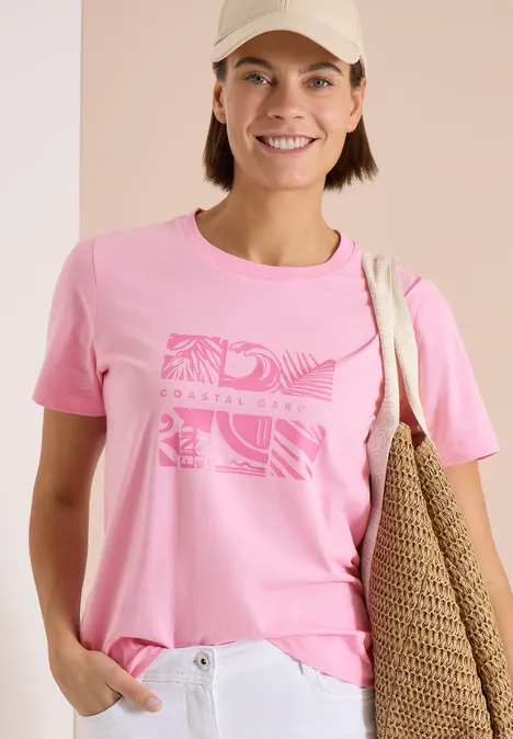 Shirt met ronde hals en frontprint flamingo rose Persoon met roze t-shirt met print, een witte broek en een strooien schoudertas.