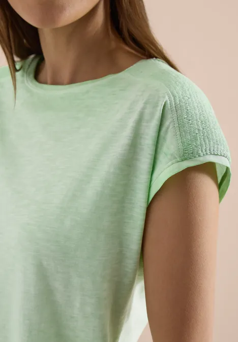 Frau in hellgrünem T-Shirt mit strukturierter Stoffpartie an den Schultern