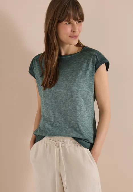 Person mit grünem T-Shirt und beiger Hose, Hände in den Taschen