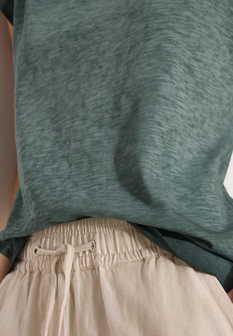 Casual-Look mit locker sitzendem, graugrünem T-Shirt und beigen, elastischen Leinenhosen – schlicht und bequem.