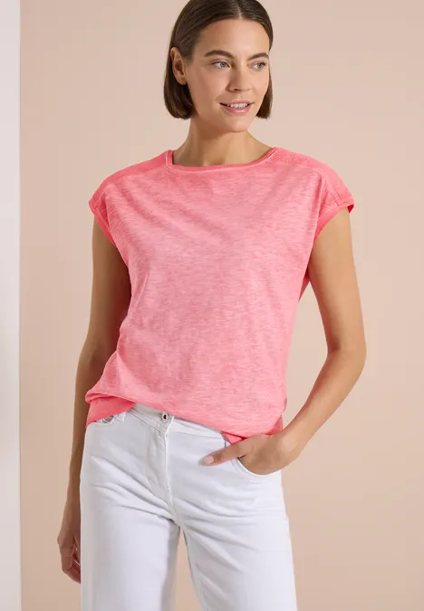 T-Shirt aus Jersey im Garment Dye Look coral Frau in pinkem T-Shirt und weißen Jeans, steht mit einer Hand in der Hosentasche.