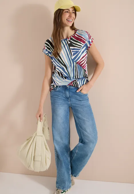 Personne porte un top rayé coloré, jean large, casquette jaune et grand sac beige.