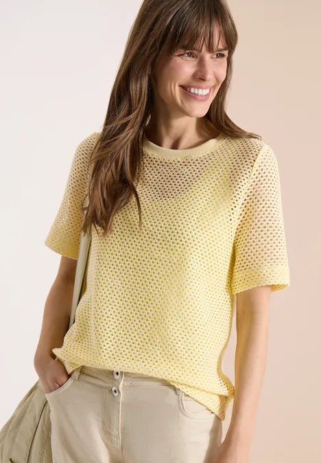 Shirt met ronde hals in ajour look buttermilk yellow Vrouw in geel gehaakt t-shirt en beige broek, handen in de zakken, nonchalant pose.