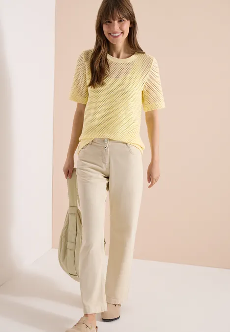 Shirt met ronde hals in ajour look buttermilk yellow Vrouw in geel T-shirt met korte mouwen en crème wijde broek, bijpassende tas, tegen lichte achtergrond.