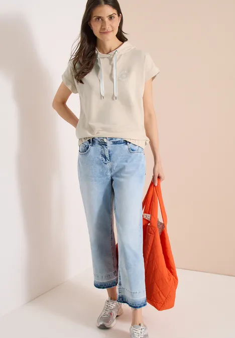 Vrouw in beige capuchonshirt en wijd lichtblauw spijkerbroek met een oranje tas.