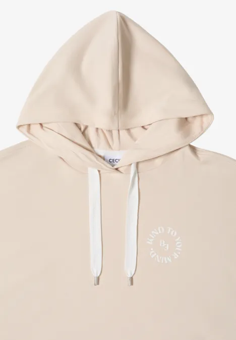Licht beige capuchontrui met witte trekkoorden en een kleine witte tekst op de borst.