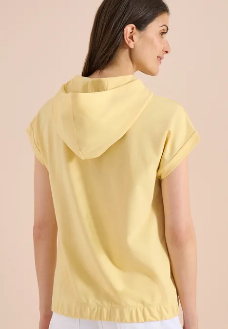 Vrouw van achteren in een lichtgele, mouwloze capuchontop.