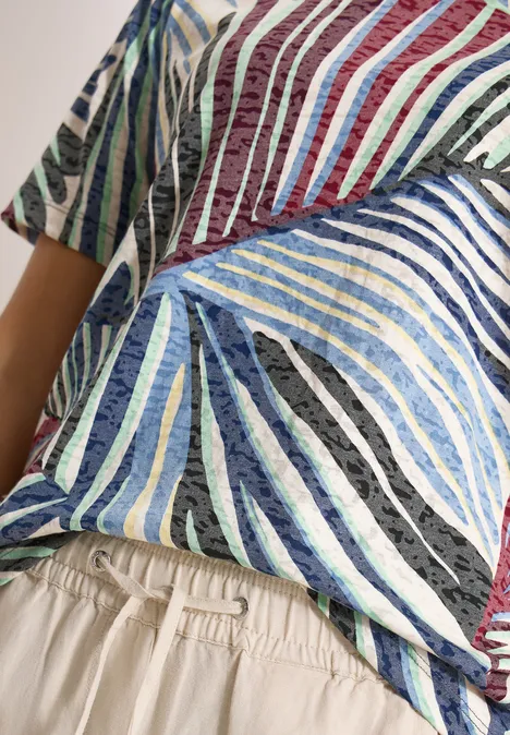Shirt in burnout-look met print palm breeze green Close-up van een torso met een kleurrijk gestreept shirt en beige broek met elastische tailleband.