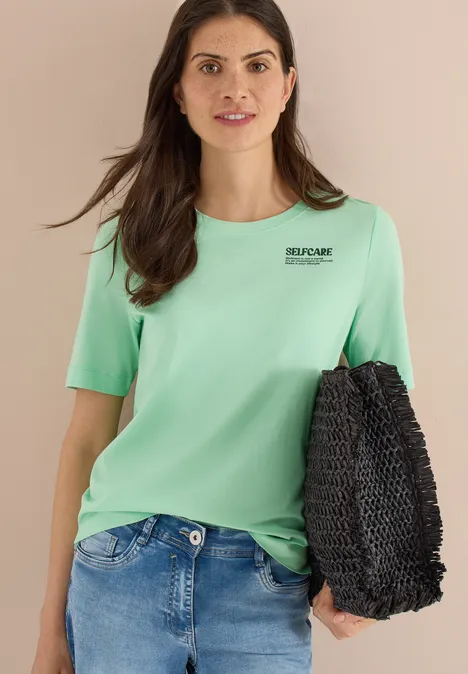 Vrouw met mintgroen T-shirt, blauwe spijkerbroek en zwarte gevlochten tas.