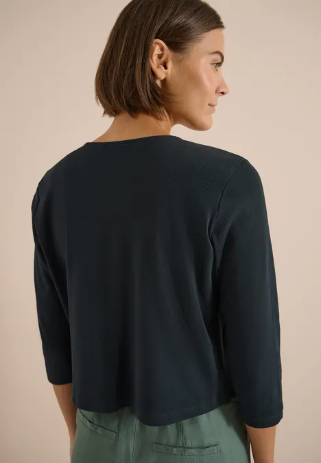 Achteraanzicht van persoon met kort bobkapsel en donkergroen kort vest met driekwartmouwen.