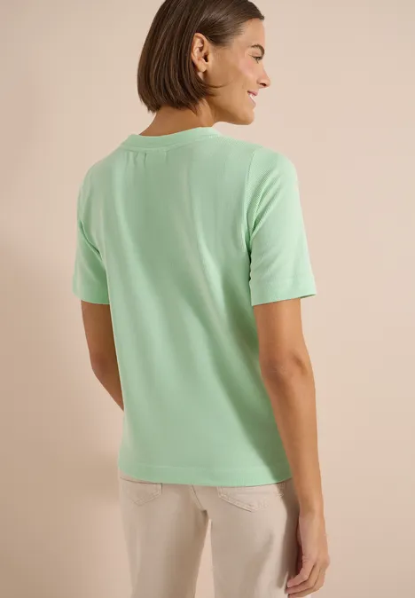 Gestreept shirt juicy lime Achteraanzicht van een vrouw in een mintgroen t-shirt en lichte broek voor een neutrale achtergrond.