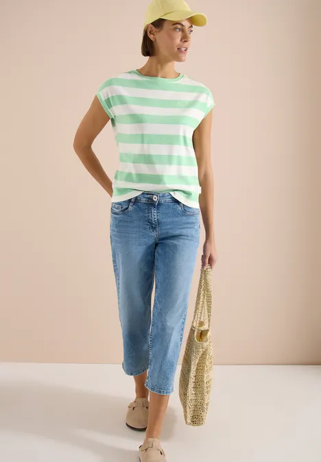 Frau in grünen-weißen Streifen-T-Shirt, hellblauen Cropped-Jeans, Sandalen und Korbtasche.