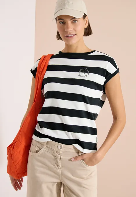 Model trägt schwarz-weiß gestreiftes T-Shirt, beige Hose, orange Tasche und Cap.