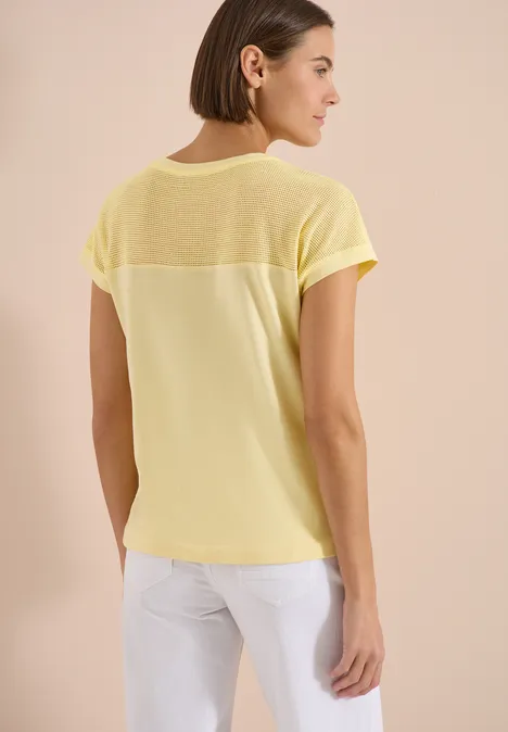 Frau von hinten in lockerem gelbem T-Shirt mit transparentem Rückenbereich.
