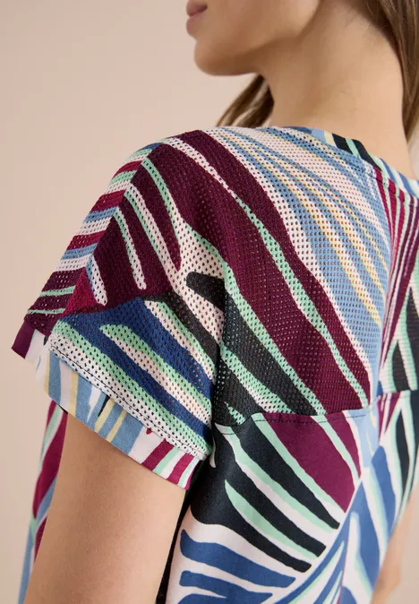 Femme de profil portant un haut en maille légère à manches courtes et rayures colorées.