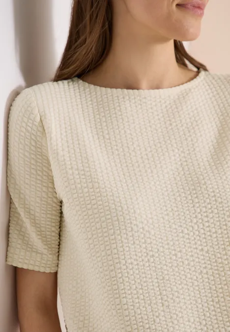 Shirt in seersucker stof pearl beige Vrouw in crèmekleurig, gebreid top met korte mouwen tegen lichte achtergrond.