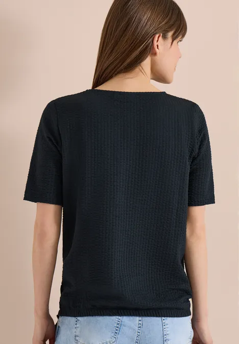 Shirt in seersucker stof palm breeze green Achteraanzicht van een vrouw in zwart T-shirt en blauwe jeans.