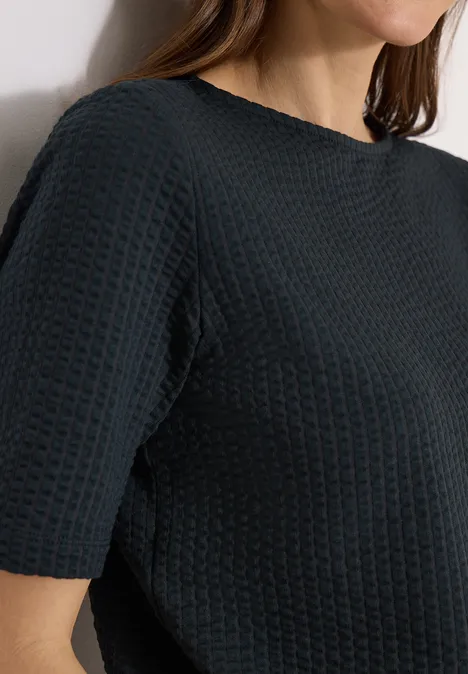 Shirt in seersucker stof palm breeze green Vrouw draagt zwart, kort mouwig topje met wafelstructuur en ronde hals.