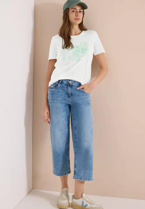 Vrouw in wit t-shirt en wijde spijkerbroek, casual look met sneakers.