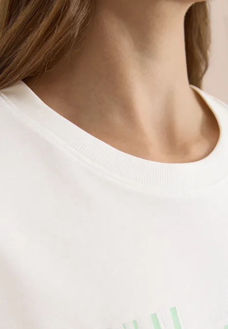 Close-up van een hals en wit T-shirt met zachtgroen motief.